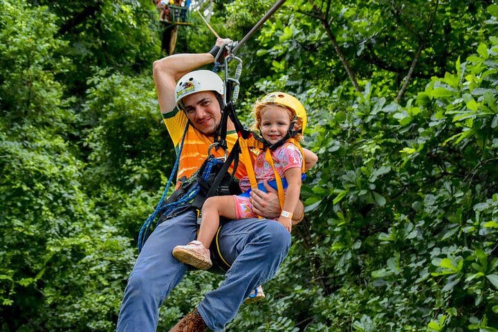 An adult and a young child zip-line along a course with the Skyline Canopy Tour.