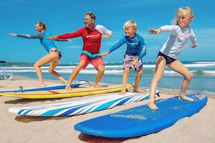 Three kids and one adult stand on beachside surf boards learning to surf with the Surf Lessons in Tamarindo, Costa Rica tour via Tripadvisor.