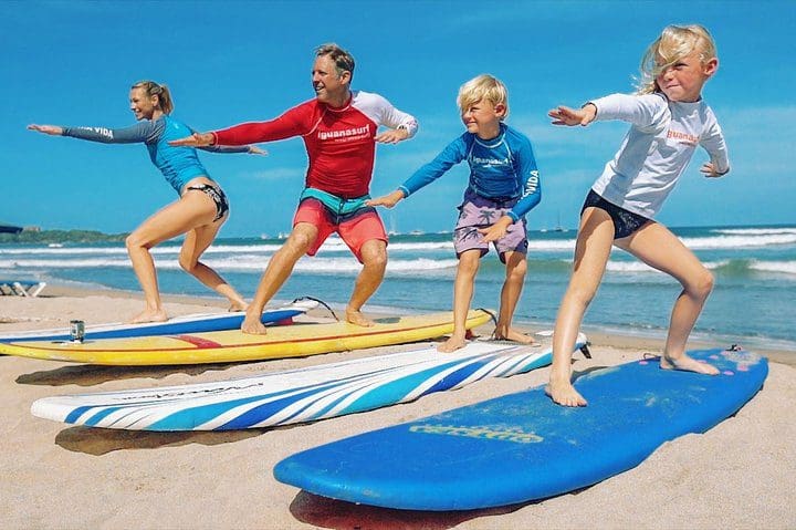 Three kids and one adult stand on beachside surf boards learning to surf with the Surf Lessons in Tamarindo, Costa Rica tour via Tripadvisor.