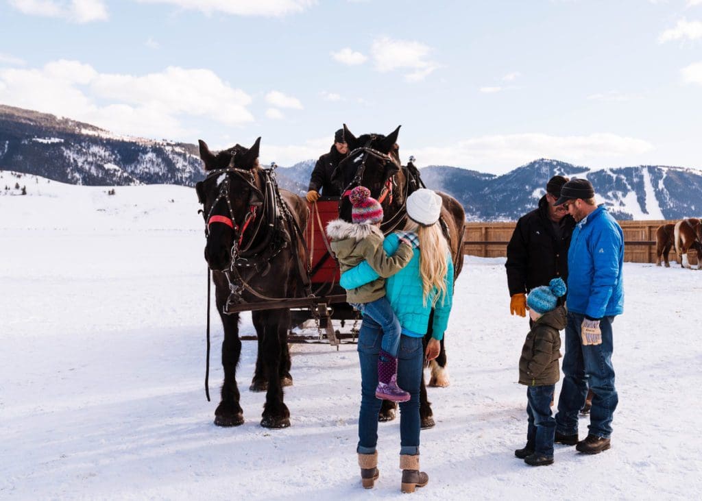 Two people gather near a horse-drawn sleigh in Jackson Hole, one of the best places for a White Christmas in the United States for families.