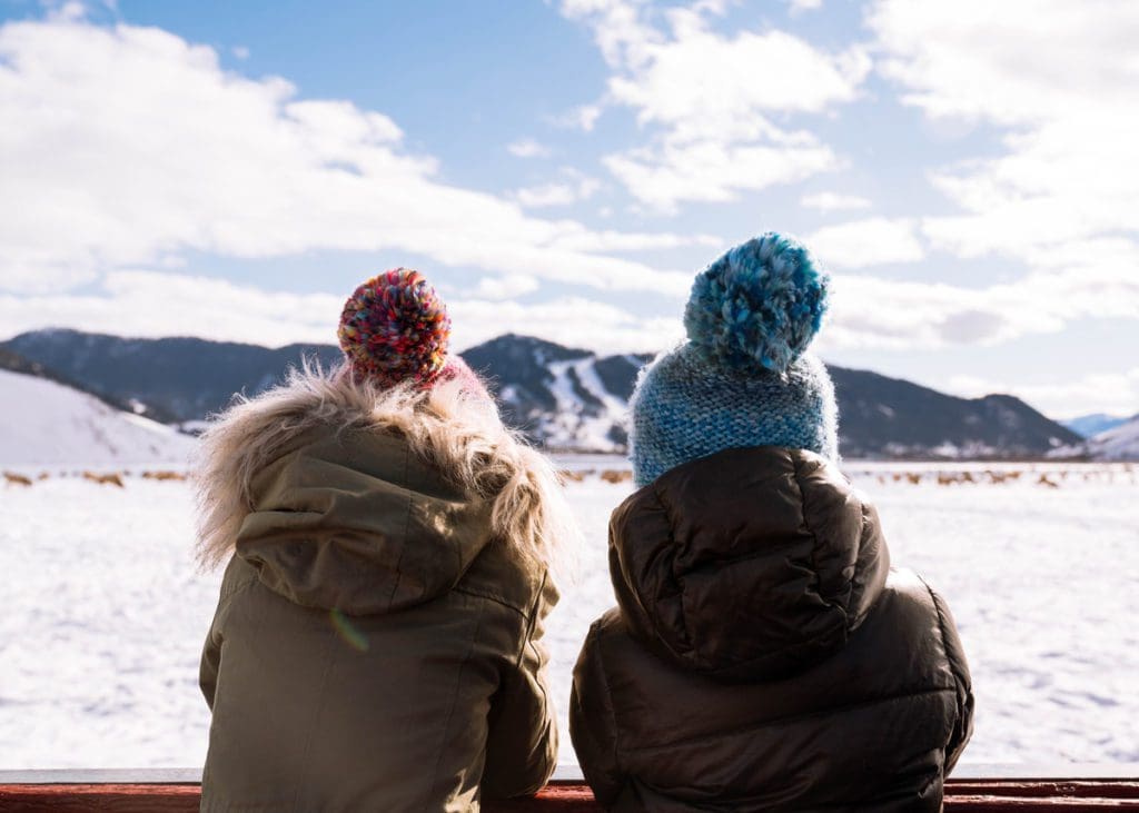 Two kids huddle together looking at the snow during Christmas at Jackson Hole, one of the best places for a White Christmas in the United States for families.