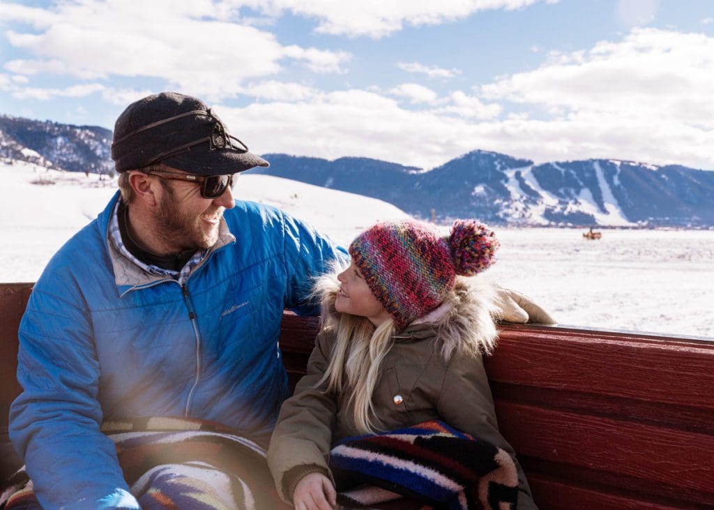 A man and his young child cuddle on a horse-drawn sleigh ride in Jackson Hole.