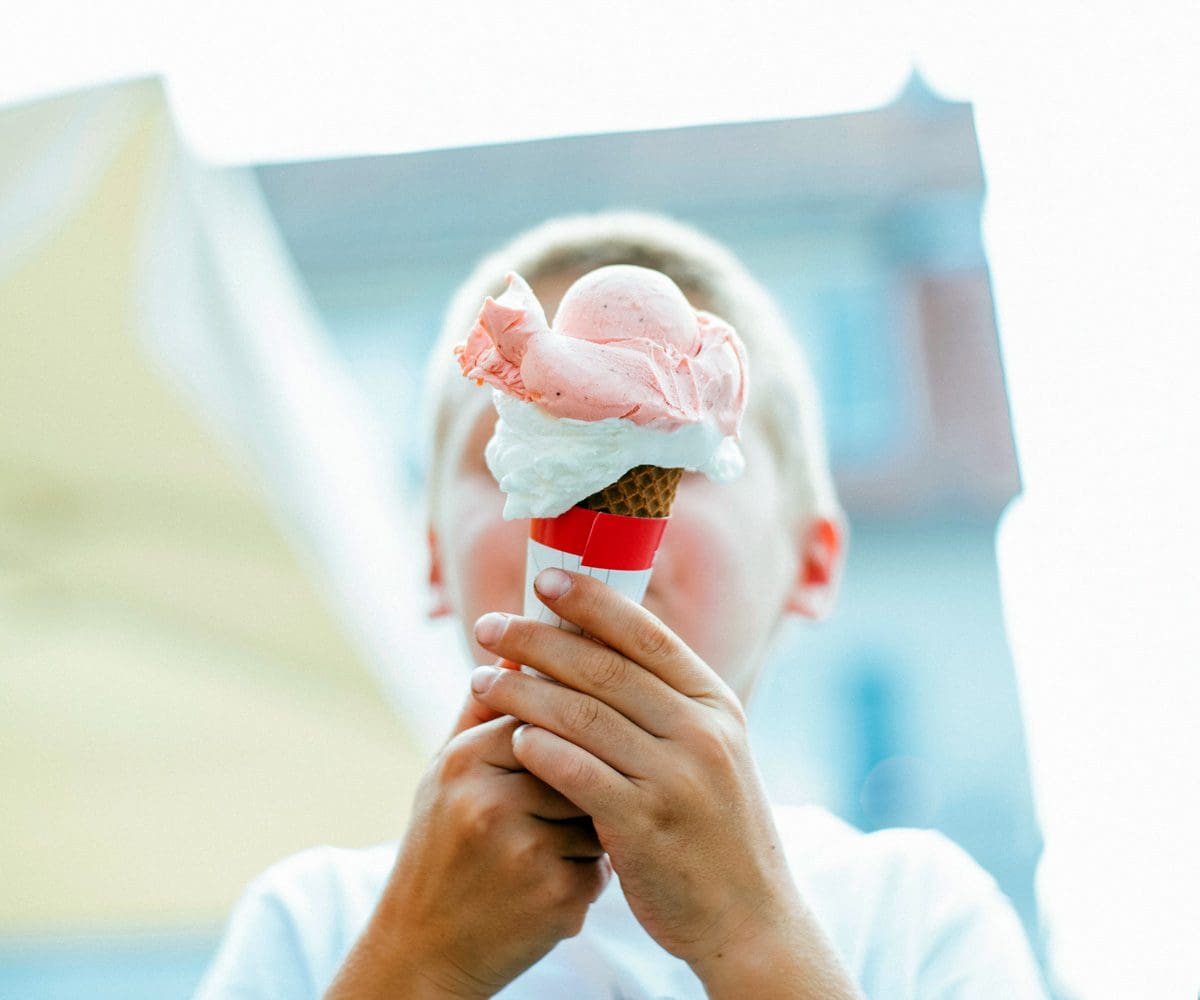 A young boy puts an ice cream cone in front of his face.