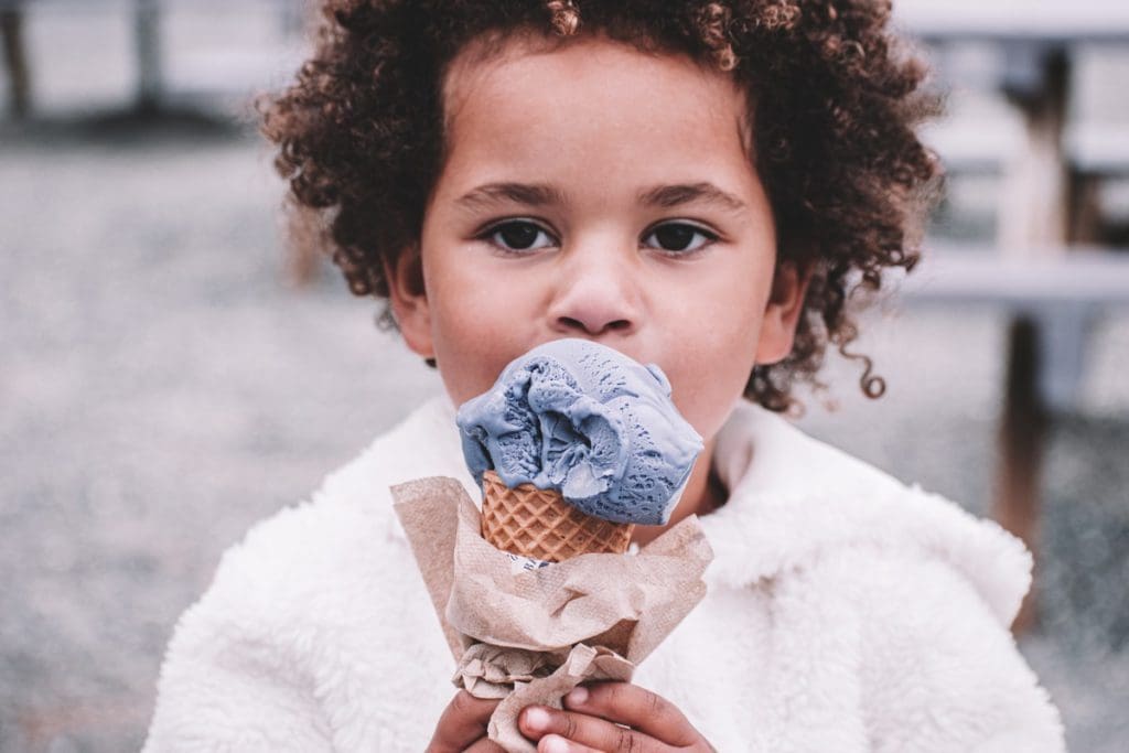 A young boy eats a large ice cream cone.