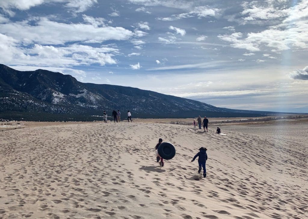 Kids play with tubes, preparing to sled down the sand dunes, at Sand Dunes National Park in Colorado, one of the best weekend getaways near Denver for families.