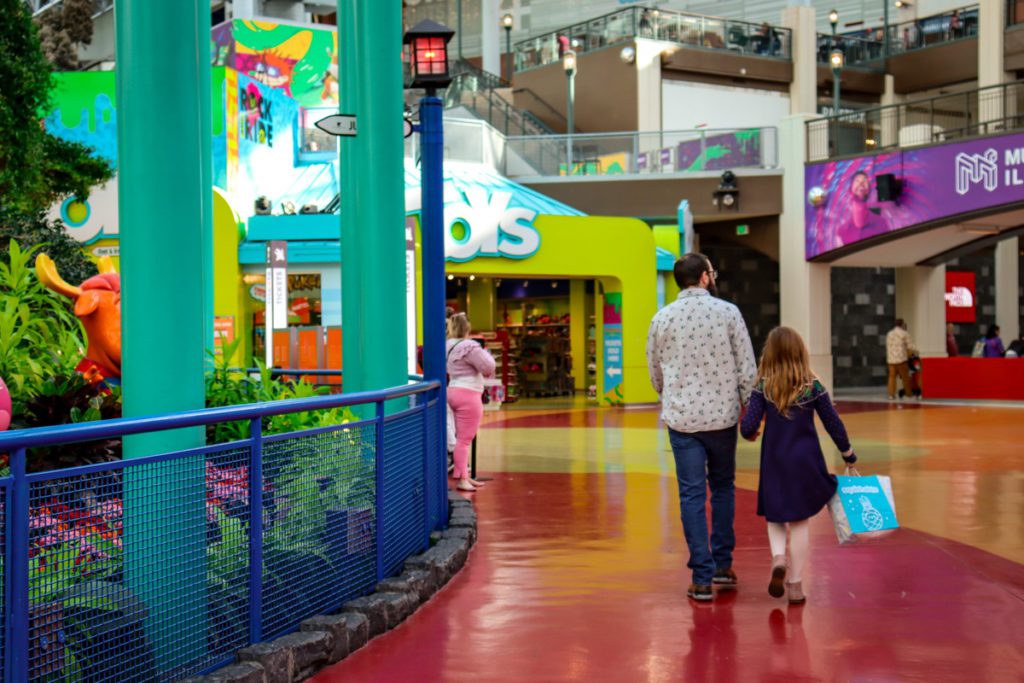 A man and his young daughter walk through Nickelodeon Universe.