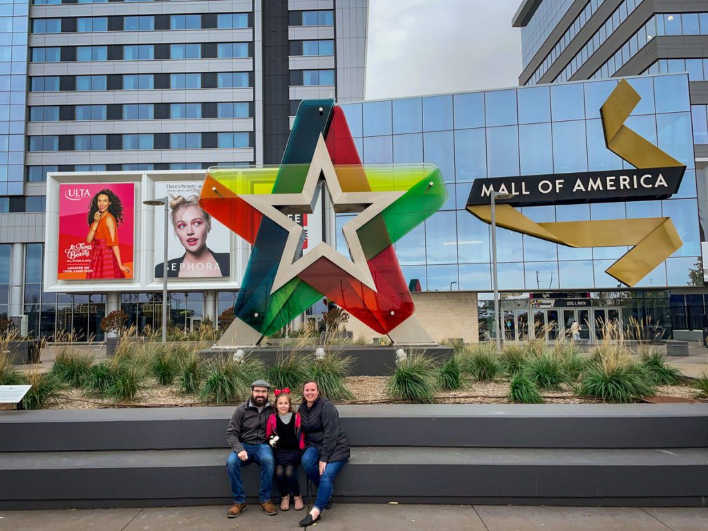 A family of three sits together outside the entrance to Mall of America.