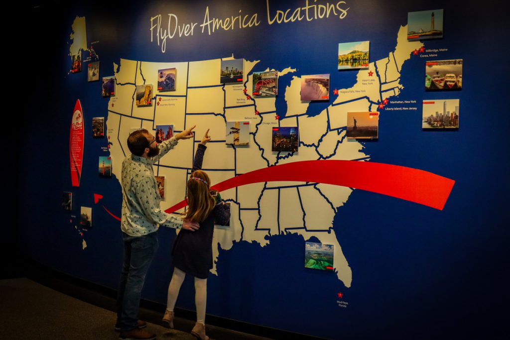 A young girl and her dad look at a map featuring the FlyOver America experience. 