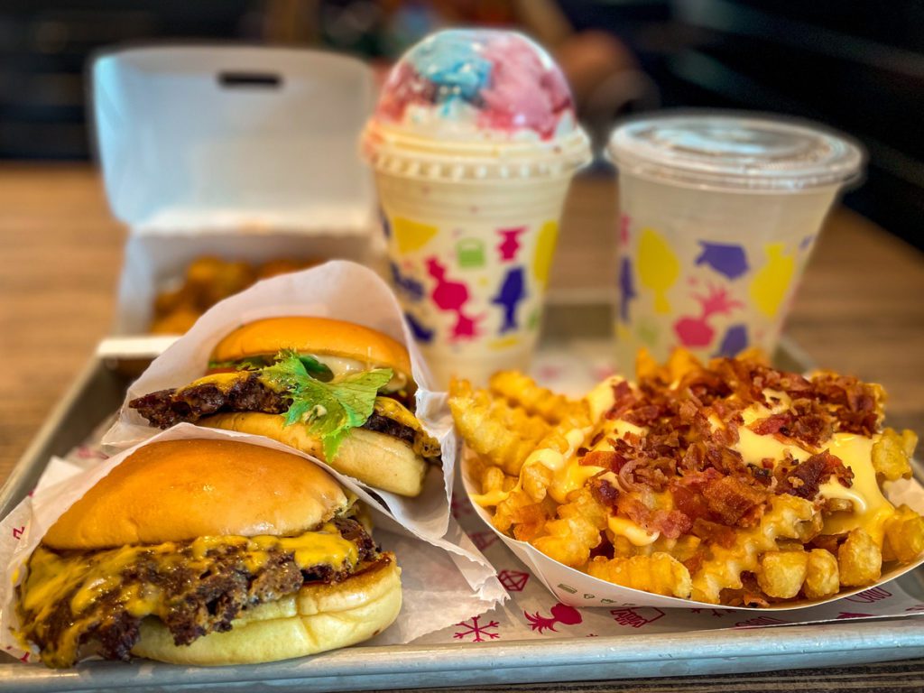 A large meal from Shake Shake, featuring burgers, fries, and a colorful shake.