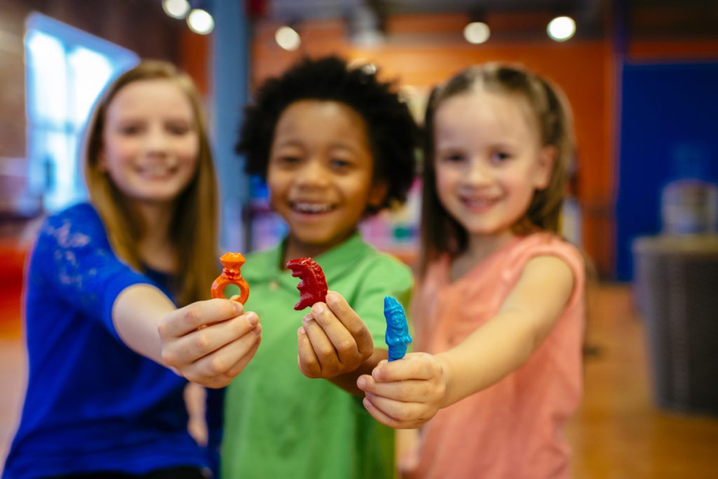 Three girls hold out molded trinkets they made at Crayola Experience. 