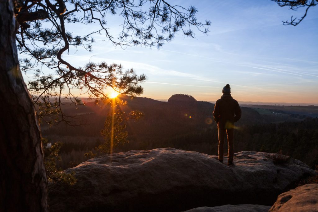 A many stands atop of cliffside looking out onto a sweeping view of Saxon Switzerland National Park at sunset.