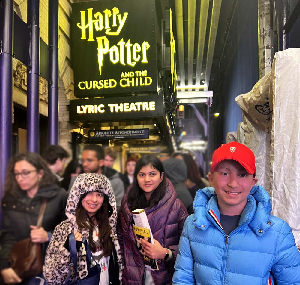 Three children standing beneath the sign for Harry Potter and The Cursed Child on Broadway.