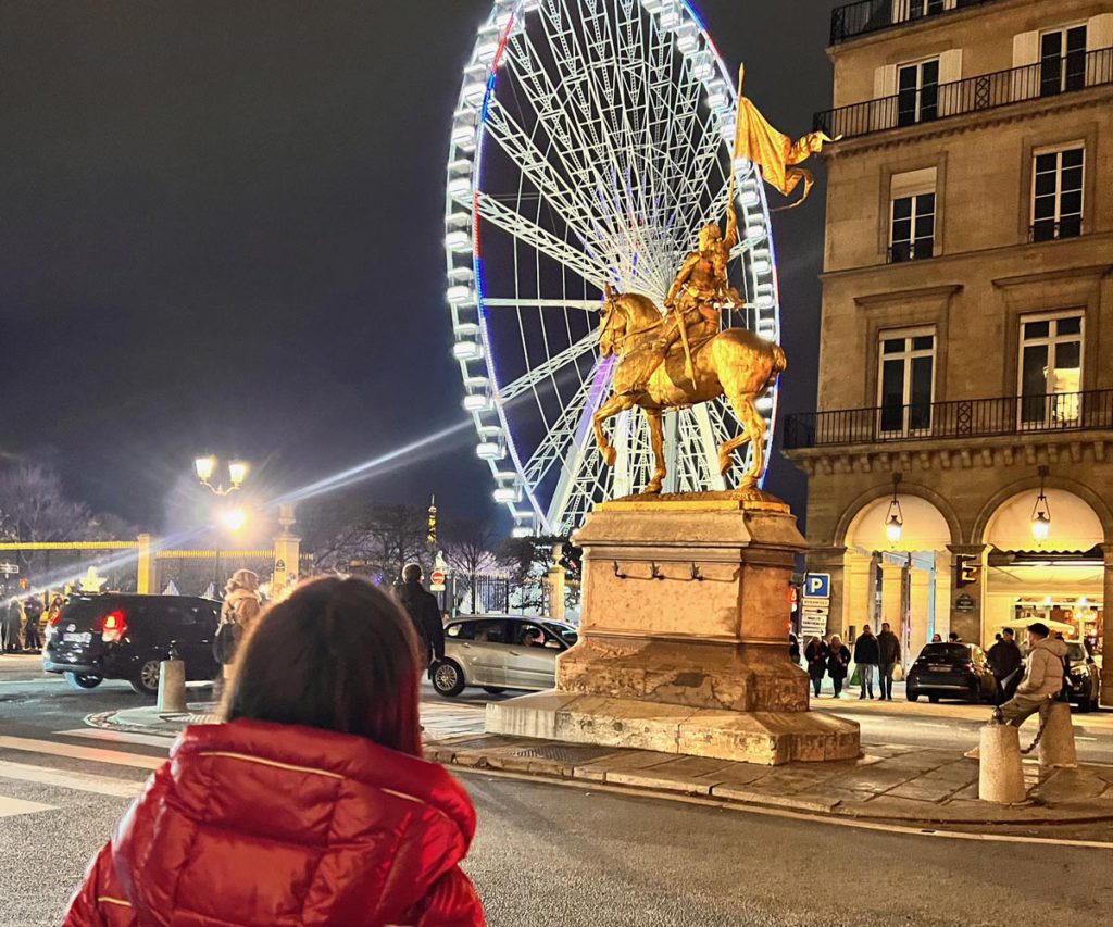 A young girl staring at a Ferris wheel in Paris. 