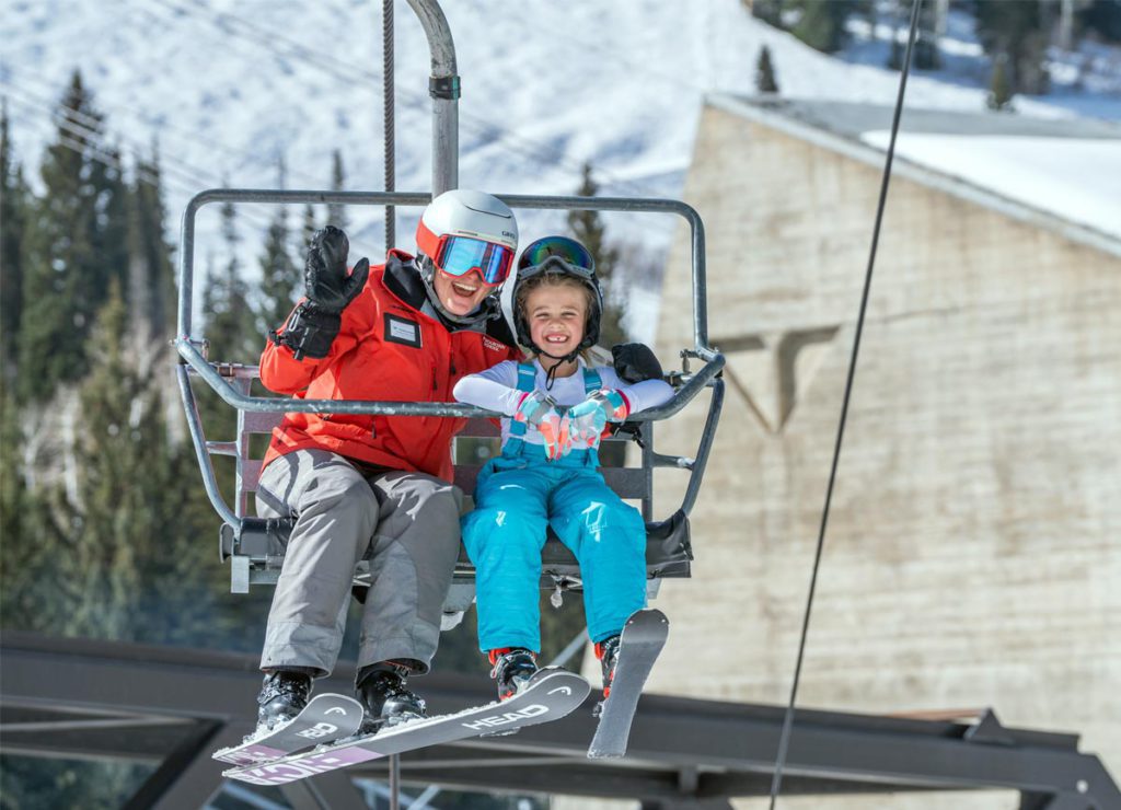 A parent and child riding a chairlift at the Snowbird Mountain School.