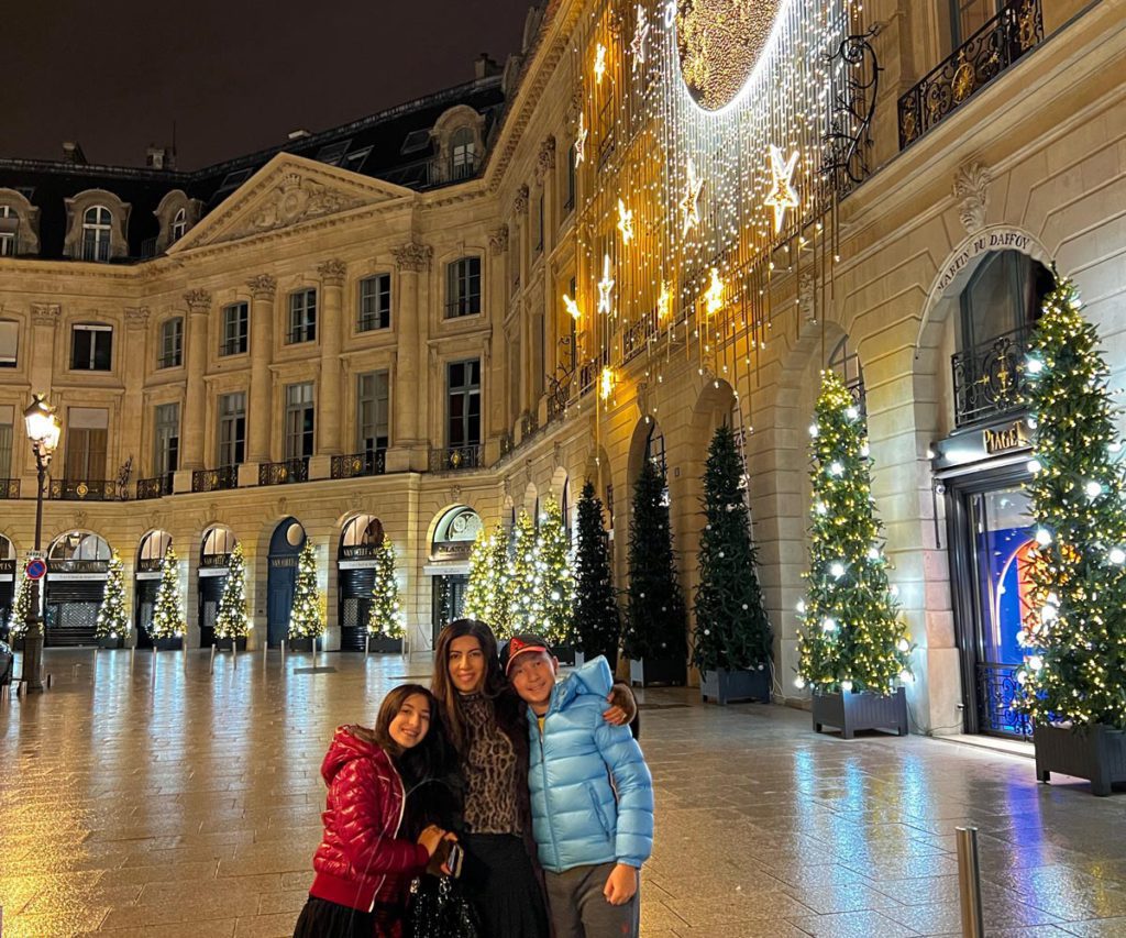 A mother and her two children posing in Paris during Christmas, surrounded by beautiful decorations.