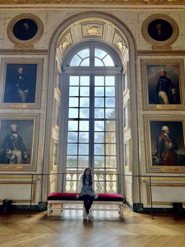 A young girl sitting on a bench inside the Palace of Versailles.