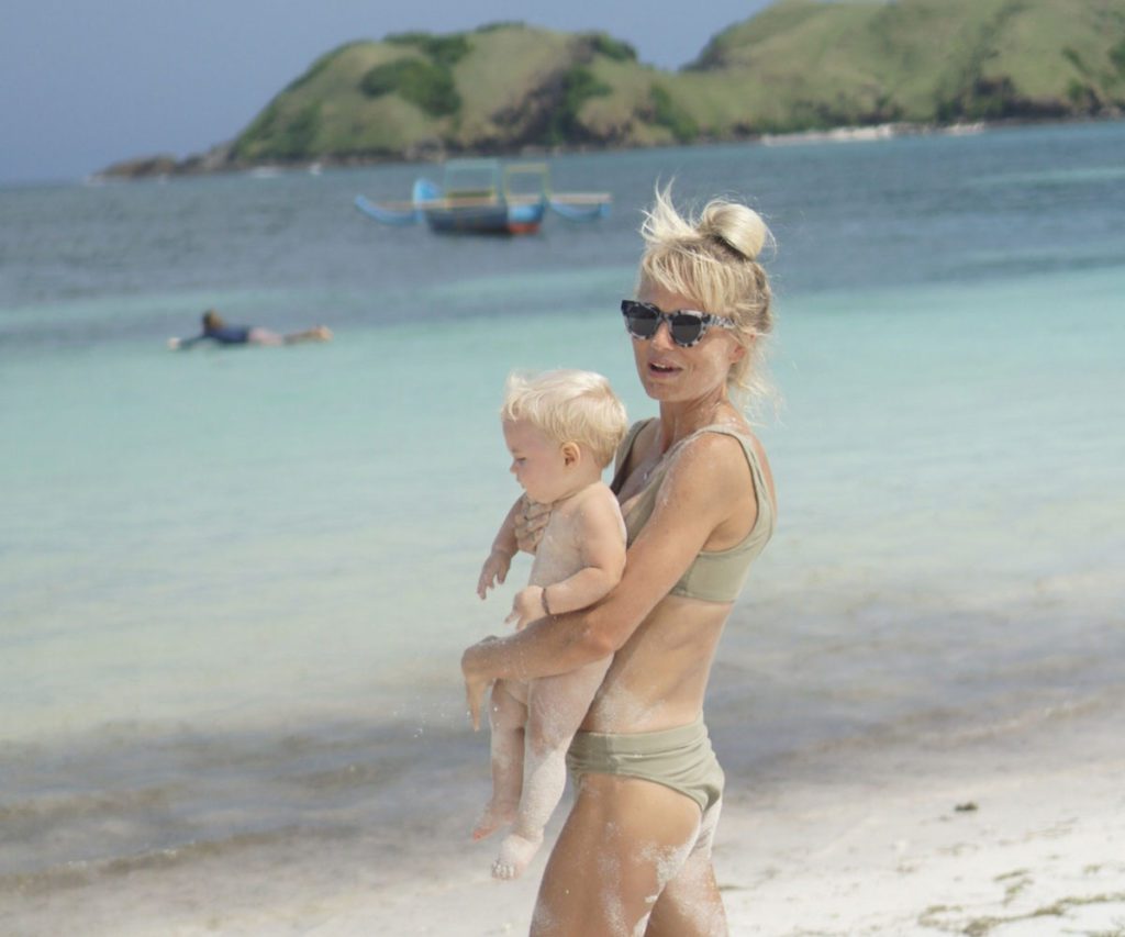 A woman holding a baby on a beach, as part of our guide to surging with kids.