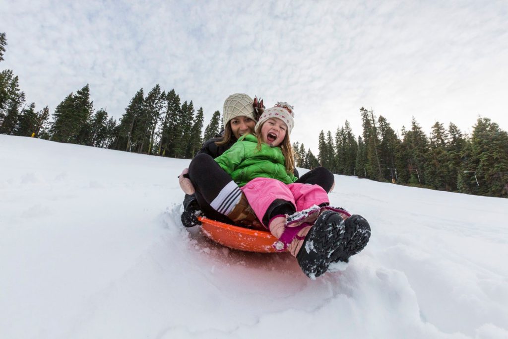 A mother and daughter on a tandem slide at Granlibakken Tahoe, one of the best places to go snow tubing in Lake Tahoe with kids.
