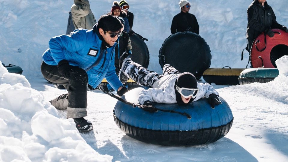 A kid preparing to snow tube at Boreal Mountain as an attendant helps.