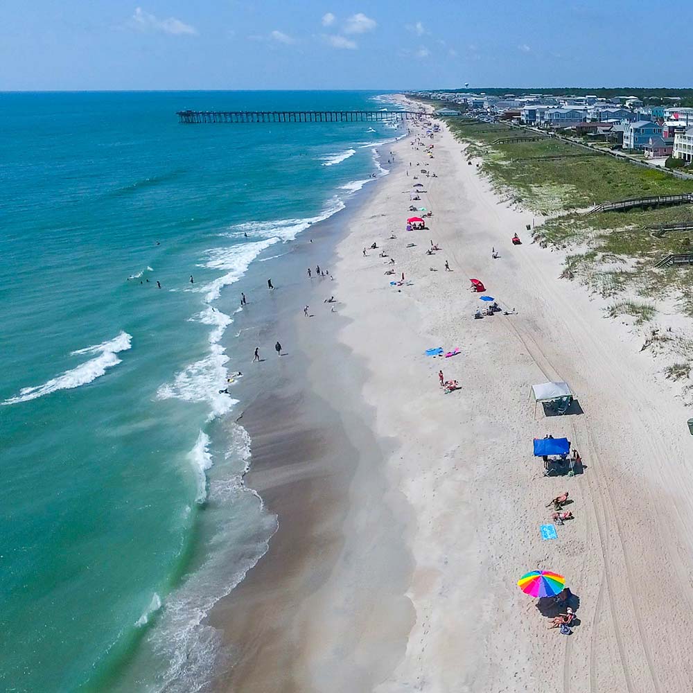 An aerial view of umbrellas and beachgoers at Kure Carolina Beach, one of the best beaches in North Carolina for families with kids. 
