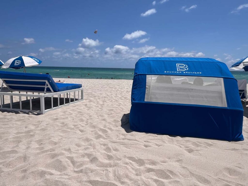 Beachfront lounge chairs and cabana with Boucher Brothers branding on the sandy shores of Loews Miami Beach Hotel.