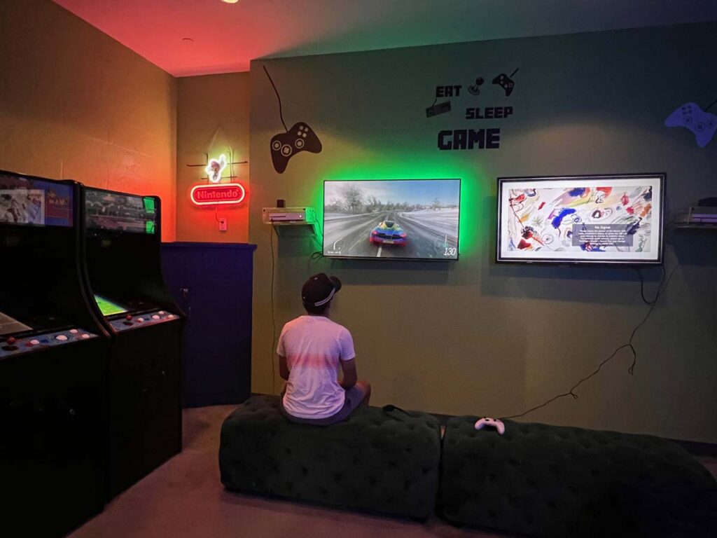 Teen enjoying video games in the game room at Loews Miami Beach Hotel, featuring arcade machines and gaming consoles.