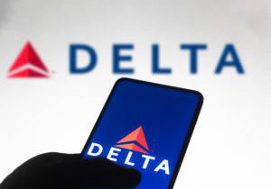 A hand navigates the Delta app with the Delta logo in the background.