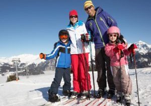 A family of four stands together on top of a mountain slope while skiing together.